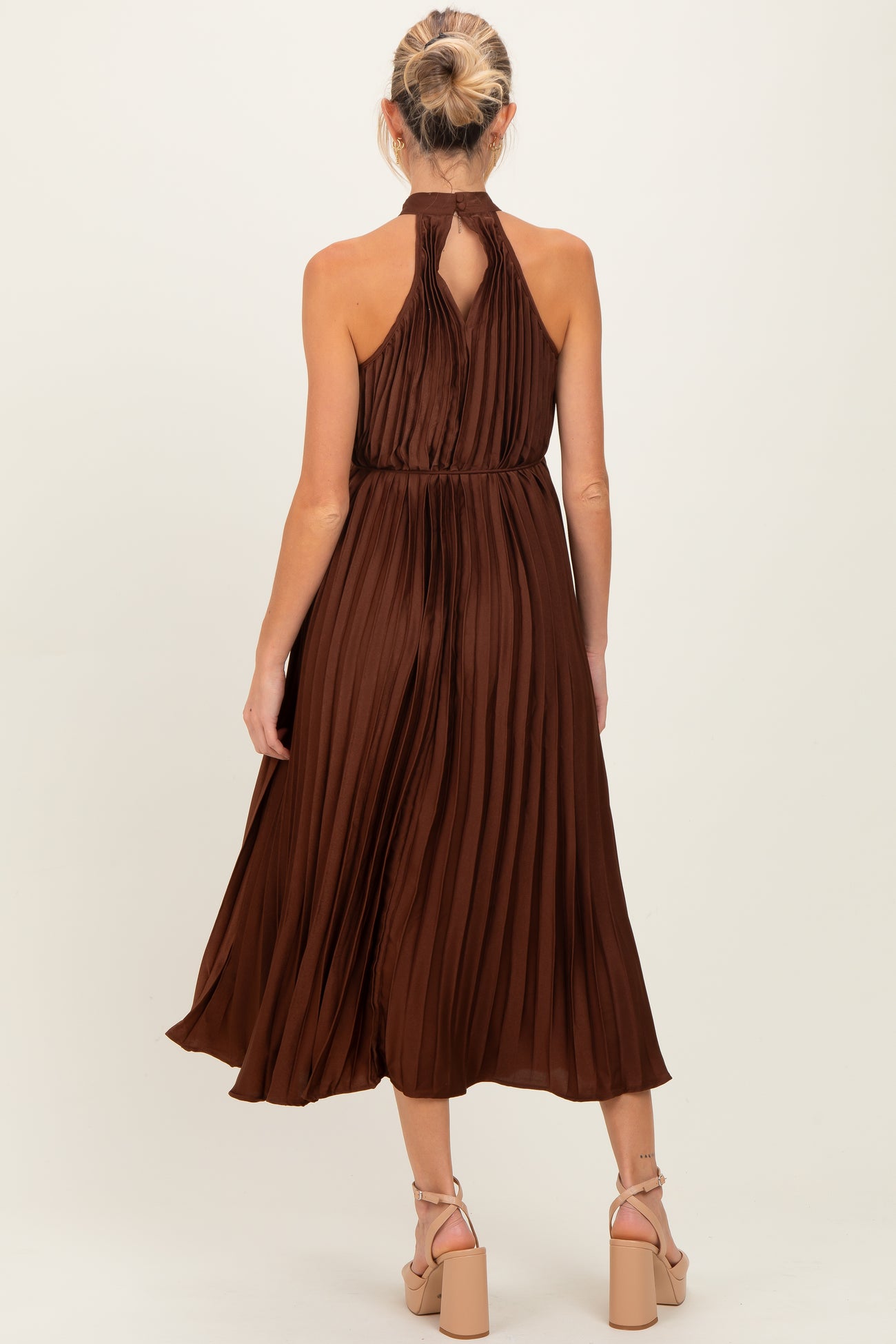 woman wearing a sleeveless brown pleated maternity dress with a halter neck and a flowy skirt, shown from the back