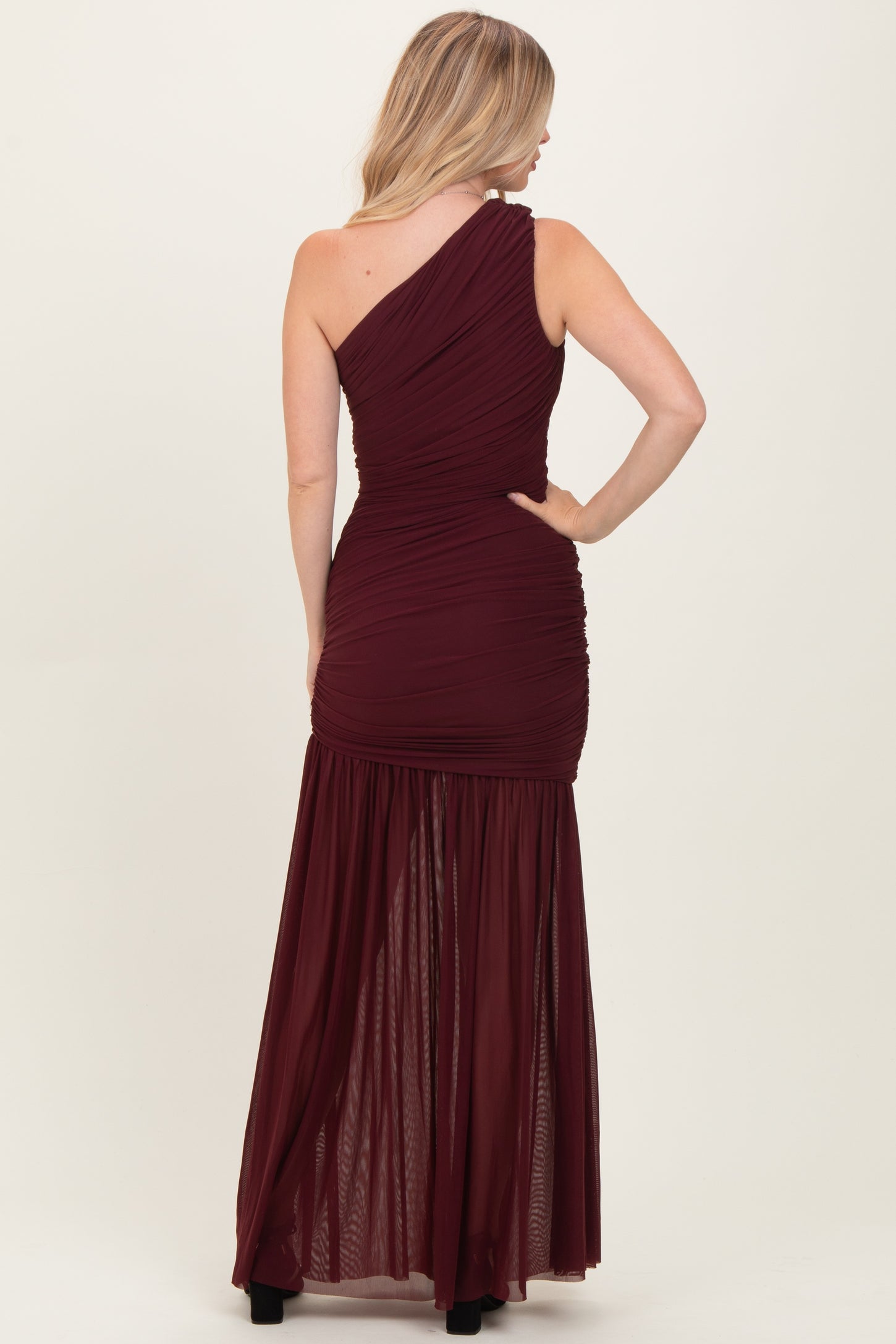 woman wearing a burgundy one-shoulder evening gown with a fitted bodice and flowing skirt