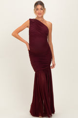 woman wearing a burgundy one-shoulder ruched maternity gown with a fitted bodice and flowing skirt, showcasing her baby bump
