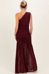 woman wearing a burgundy one-shoulder maternity gown with ruching and a flowy skirt, showing baby bump from behind