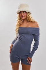 woman wearing a light blue off-shoulder long sleeve romper with ribbed detailing and a cream-colored hat