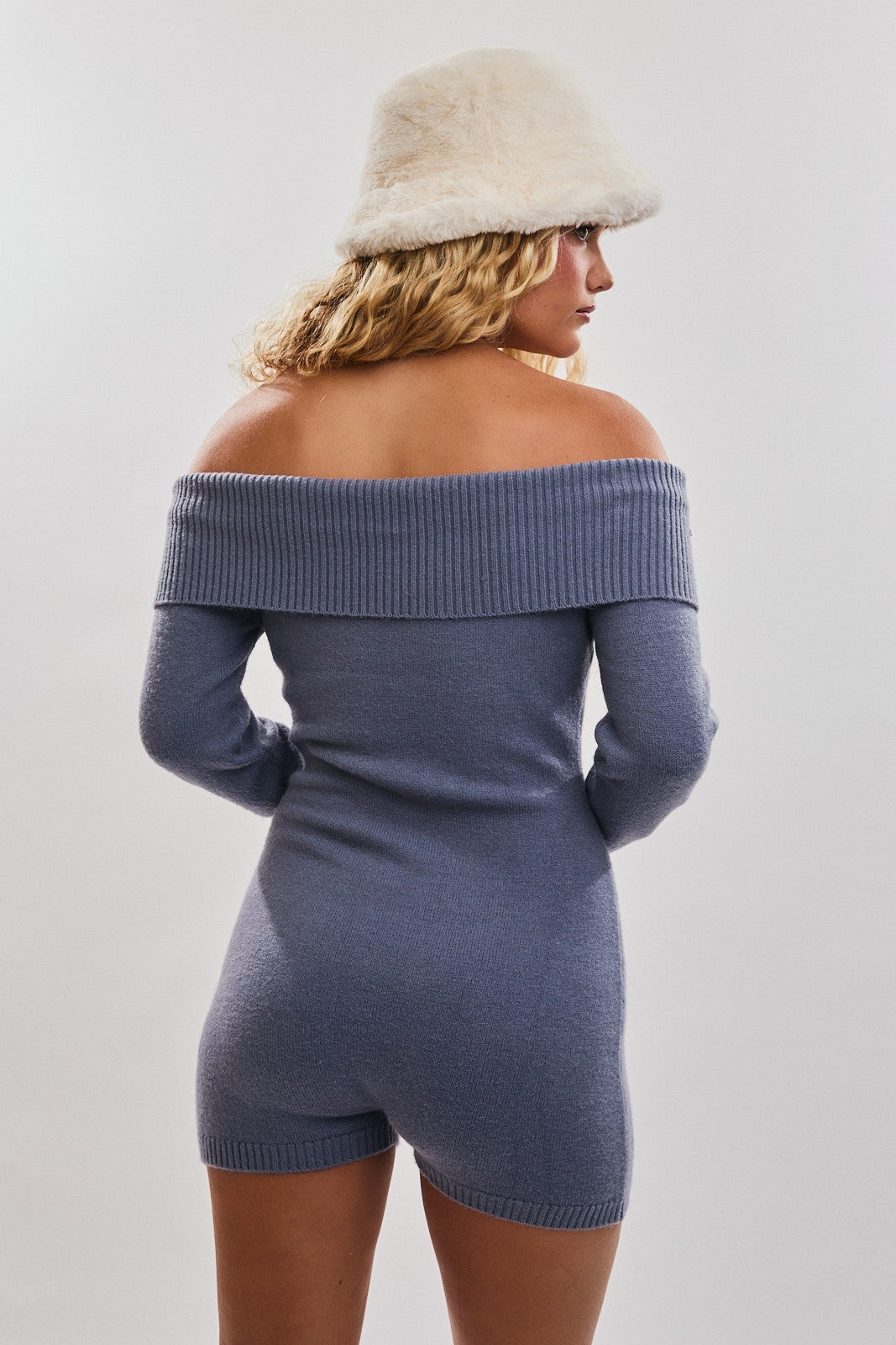 woman wearing a blue off-shoulder sweater dress with long sleeves and ribbed detailing, paired with a fluffy white hat