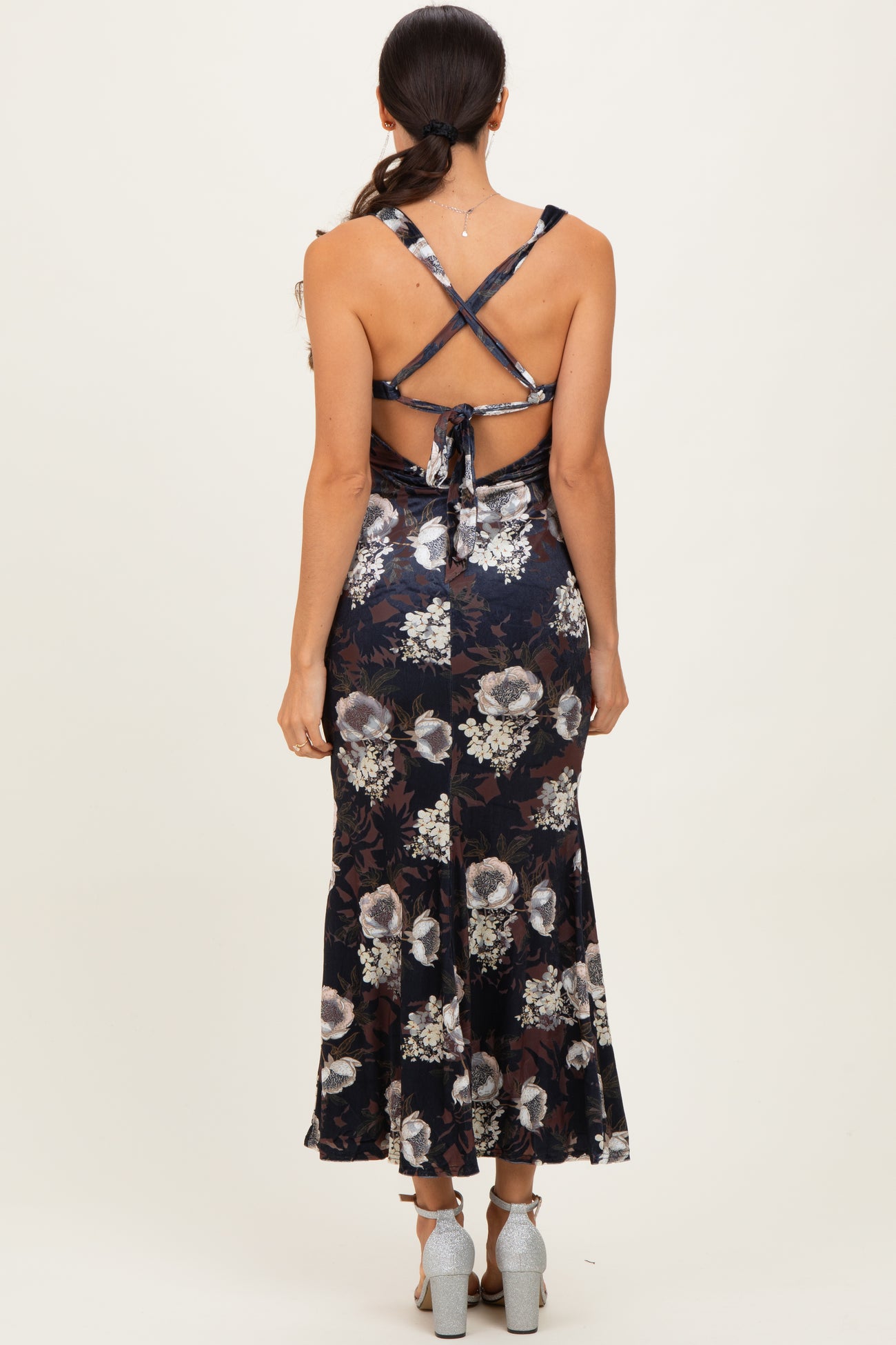 woman wearing a navy floral maxi dress with crisscross straps and a flared hem, showing the back view