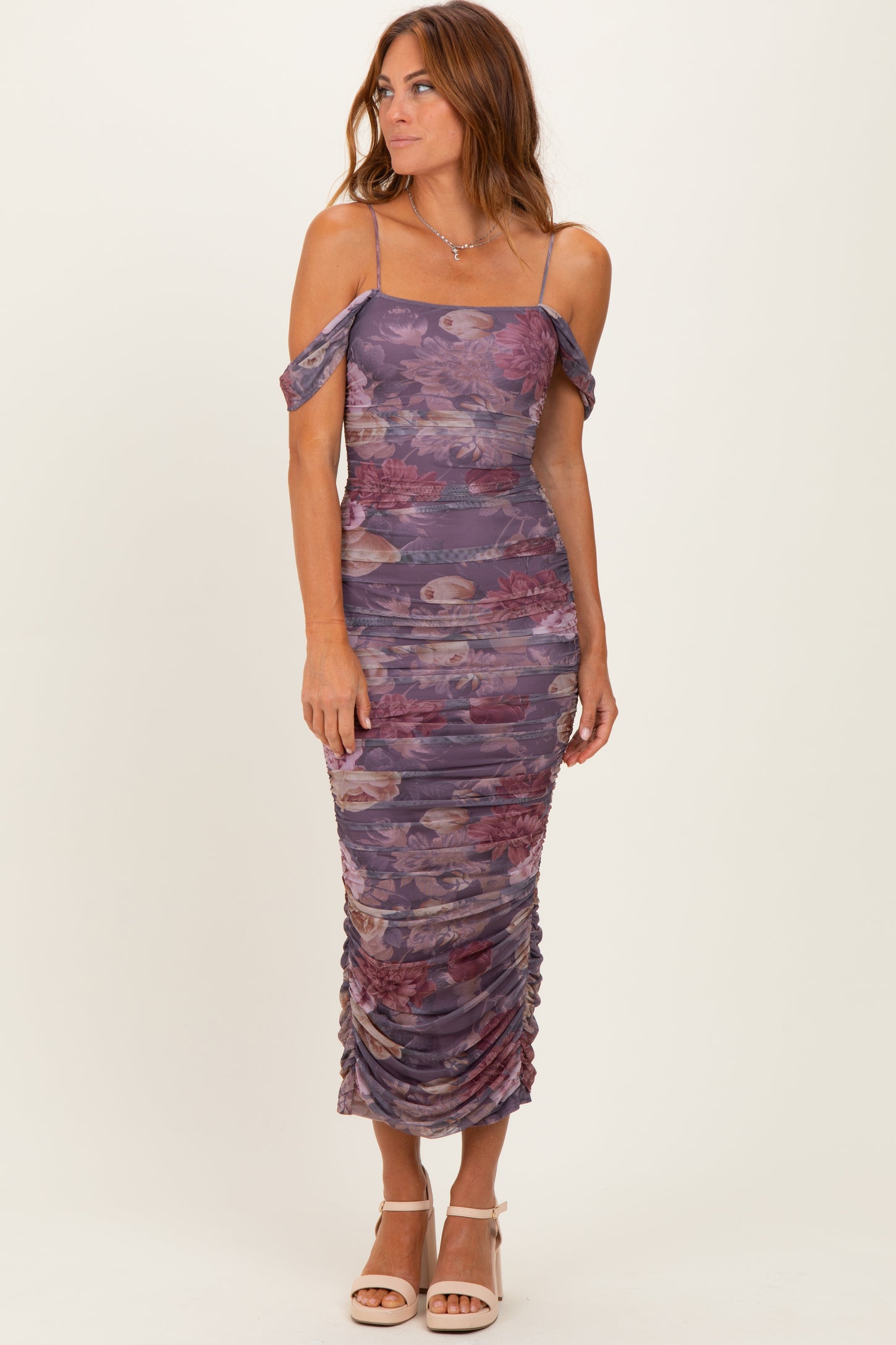 woman wearing a purple floral ruched midi dress with off-shoulder straps and side slits