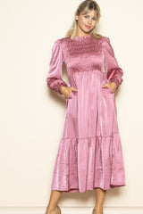 woman wearing a pink satin smocked long sleeve dress with pockets and a tiered skirt
