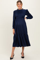 woman wearing a navy blue maternity dress with smocking details and long sleeves, showcasing her baby bump
