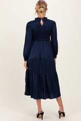 woman wearing a navy blue long sleeve maternity dress with smocking and a tiered skirt, viewed from the back