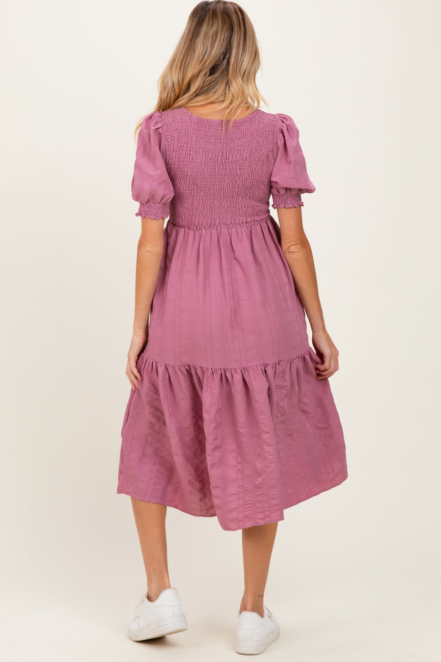 woman wearing a pink maternity dress with puff sleeves and tiered skirt, showing her back