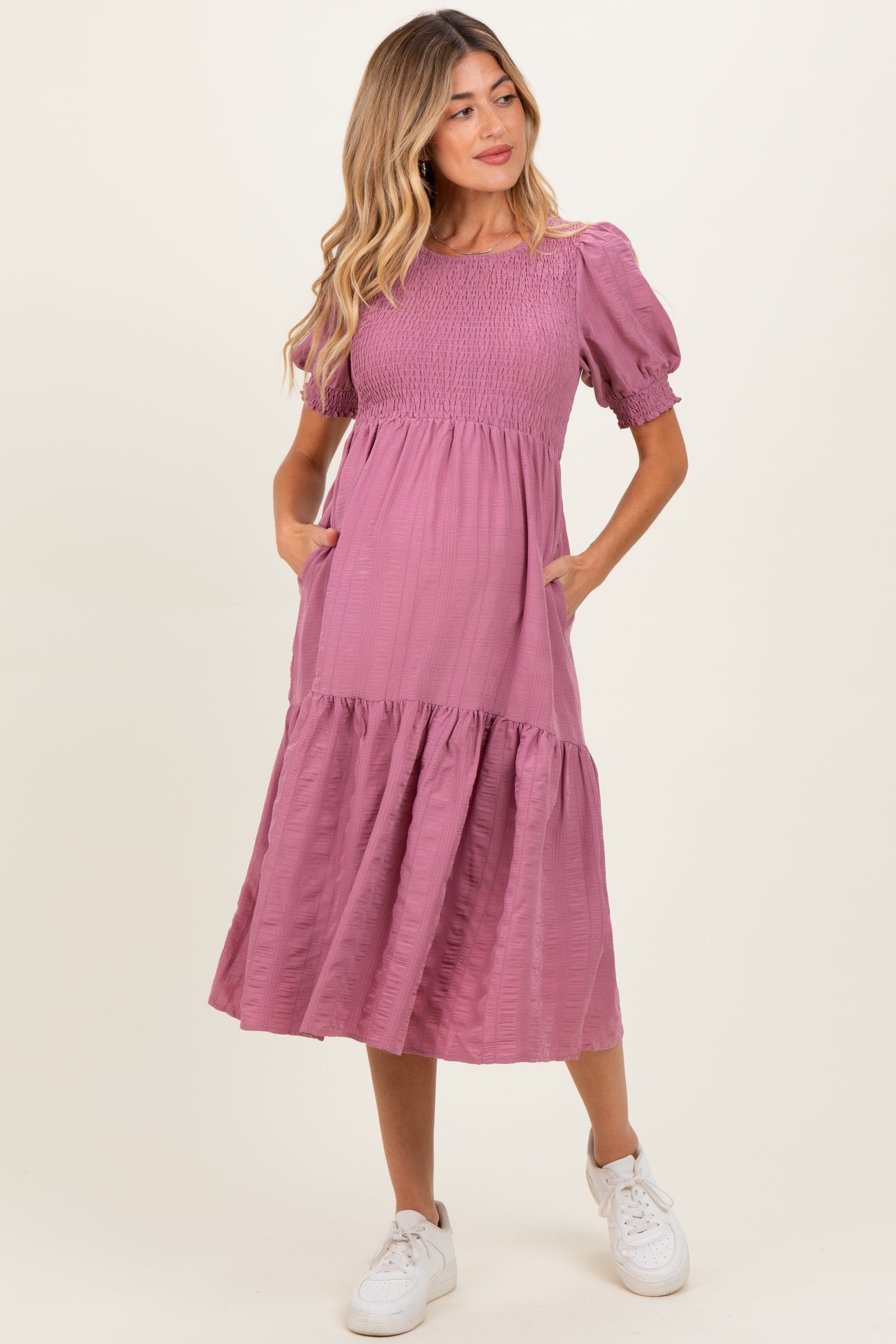 woman wearing a mauve maternity dress with puff sleeves, tiered skirt, and pockets, showcasing her baby bump