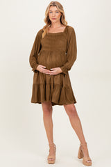 woman wearing a brown long sleeve maternity dress with a smocked bodice and ruffled hem, holding her baby bump