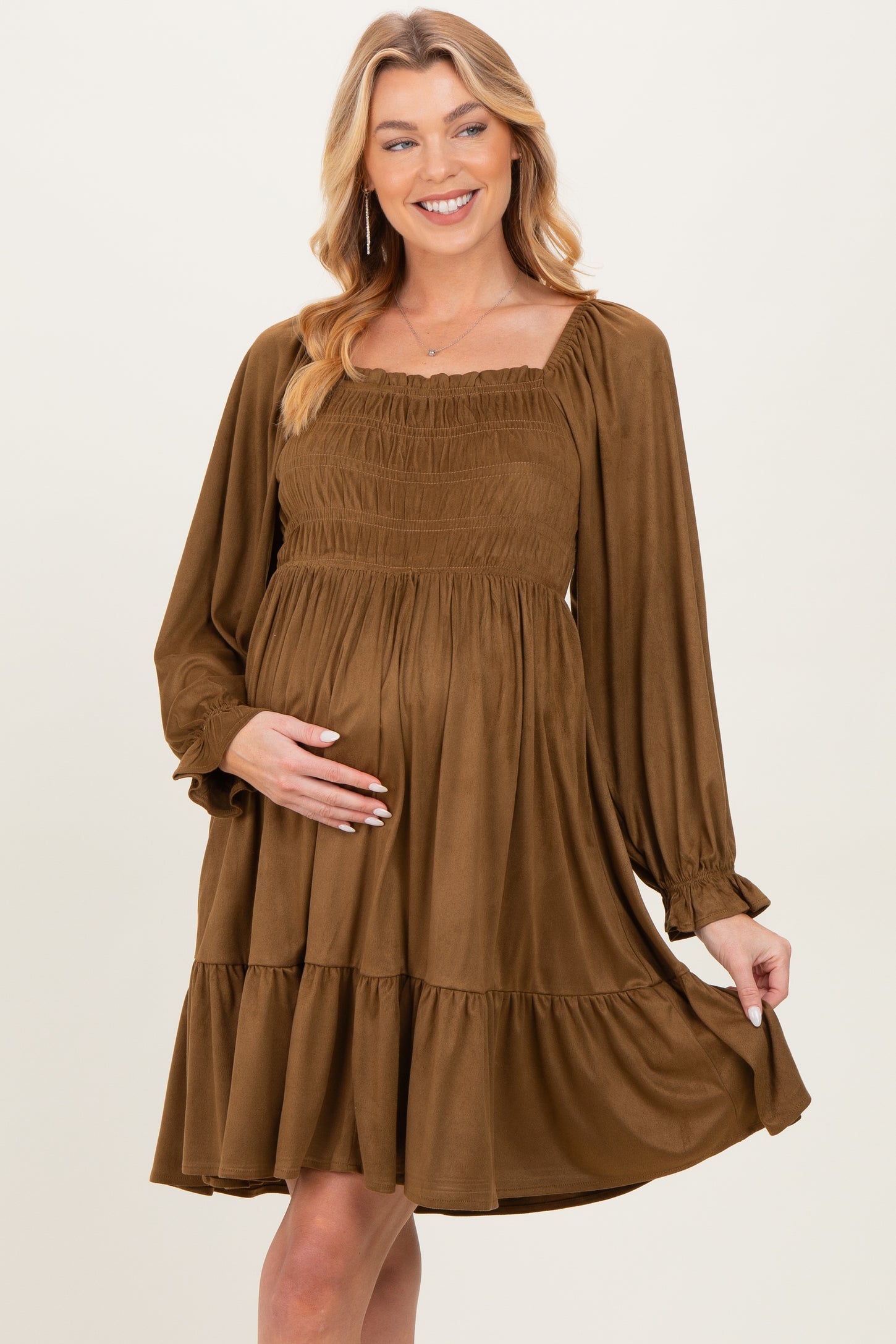woman wearing a brown maternity dress with smocked bodice and tiered skirt, gently cradling her baby bump
