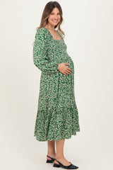 woman wearing a green floral maternity dress with long sleeves and a tiered skirt, holding her baby bump