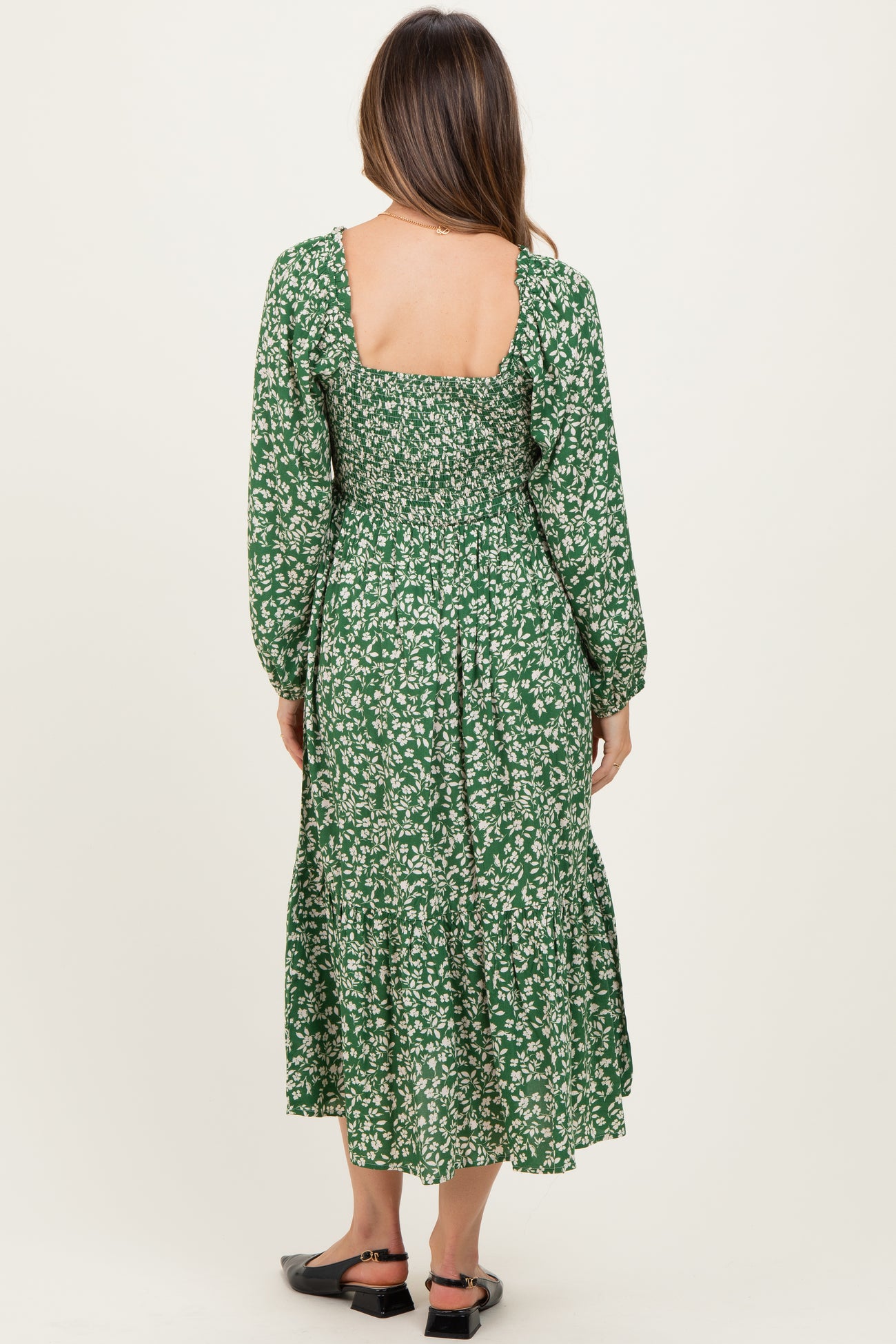 woman wearing a green floral print maternity dress with long sleeves and ruffled hem, showing the back view