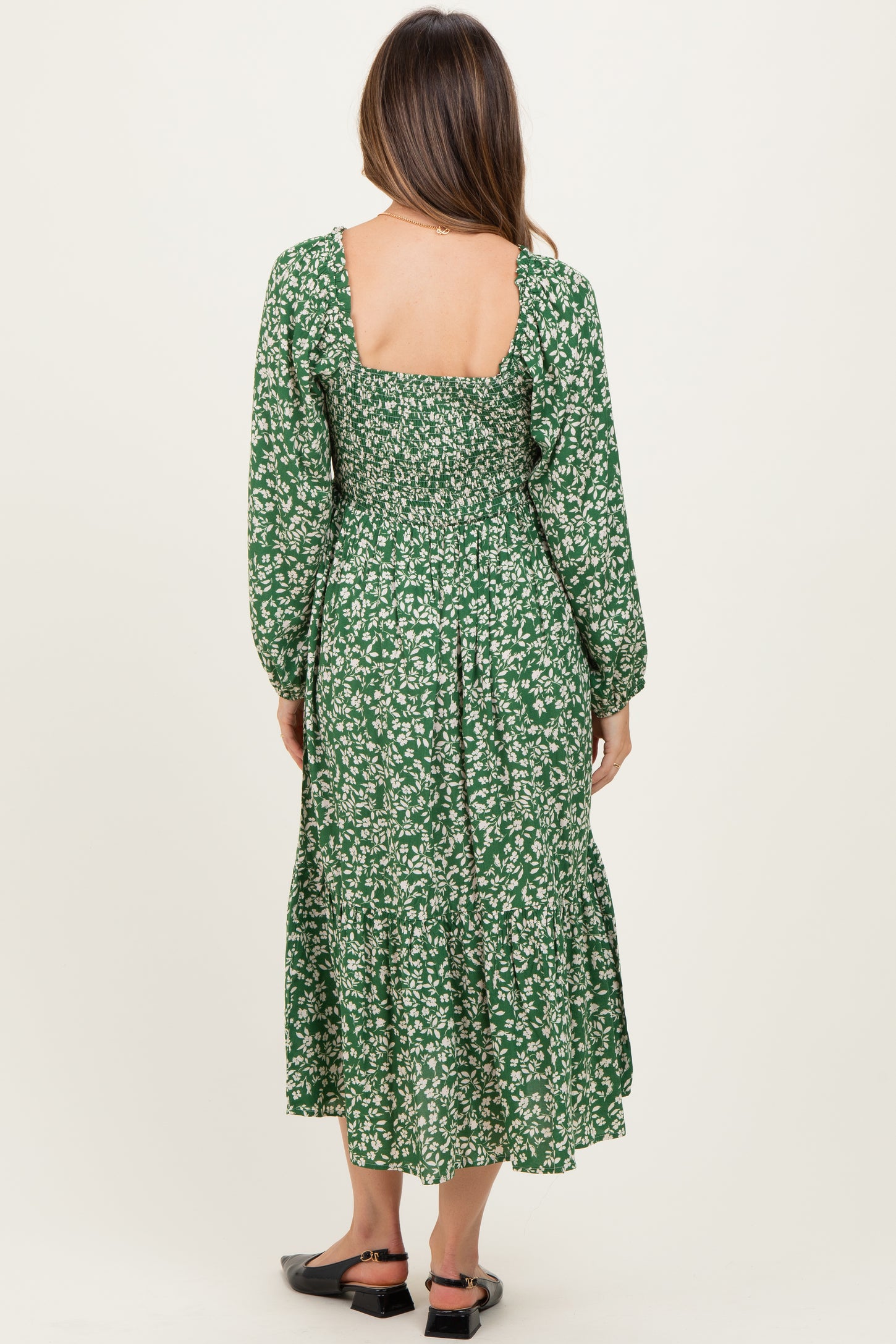 woman wearing a green floral print maternity dress with long sleeves and ruffled hem, showing the back view