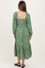 woman wearing a green floral print maternity dress with long sleeves and ruffled hem, showing the back view