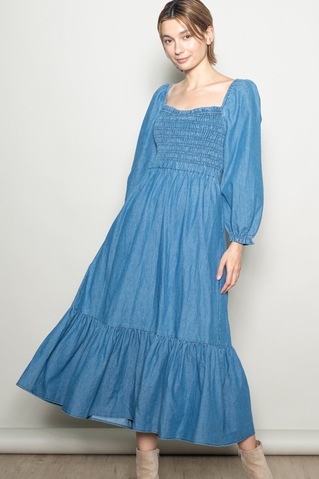 woman wearing a blue denim maxi dress with puff sleeves and a smocked bodice, standing against a neutral background