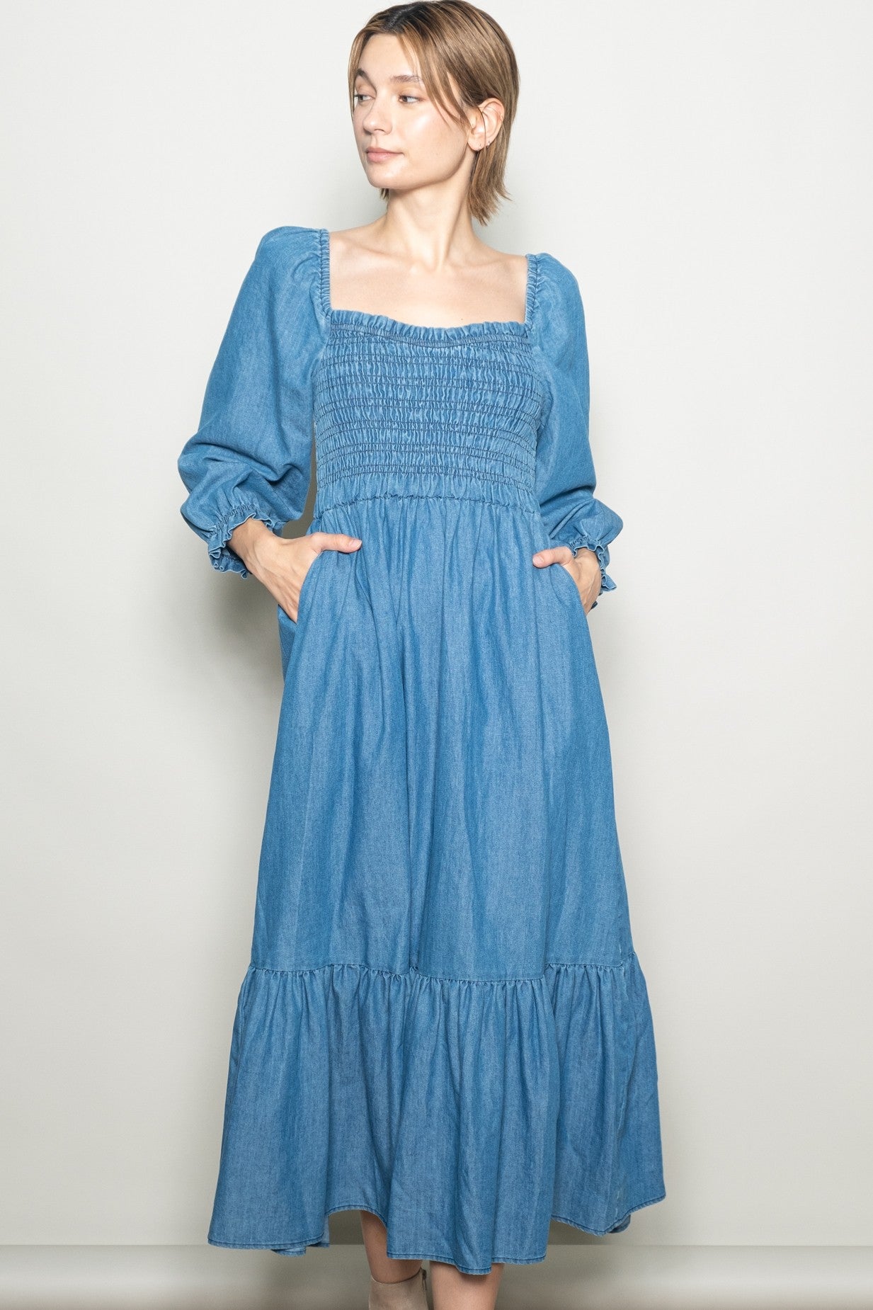 woman wearing a light blue long sleeve denim maxi dress with a smocked bodice and pockets
