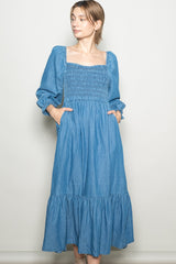 woman wearing a light blue long sleeve denim maxi dress with a smocked bodice and pockets