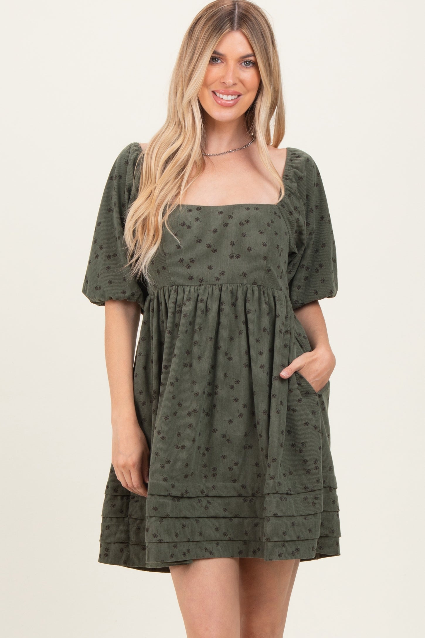 woman wearing a dark green short puff sleeve dress with a square neckline and pockets