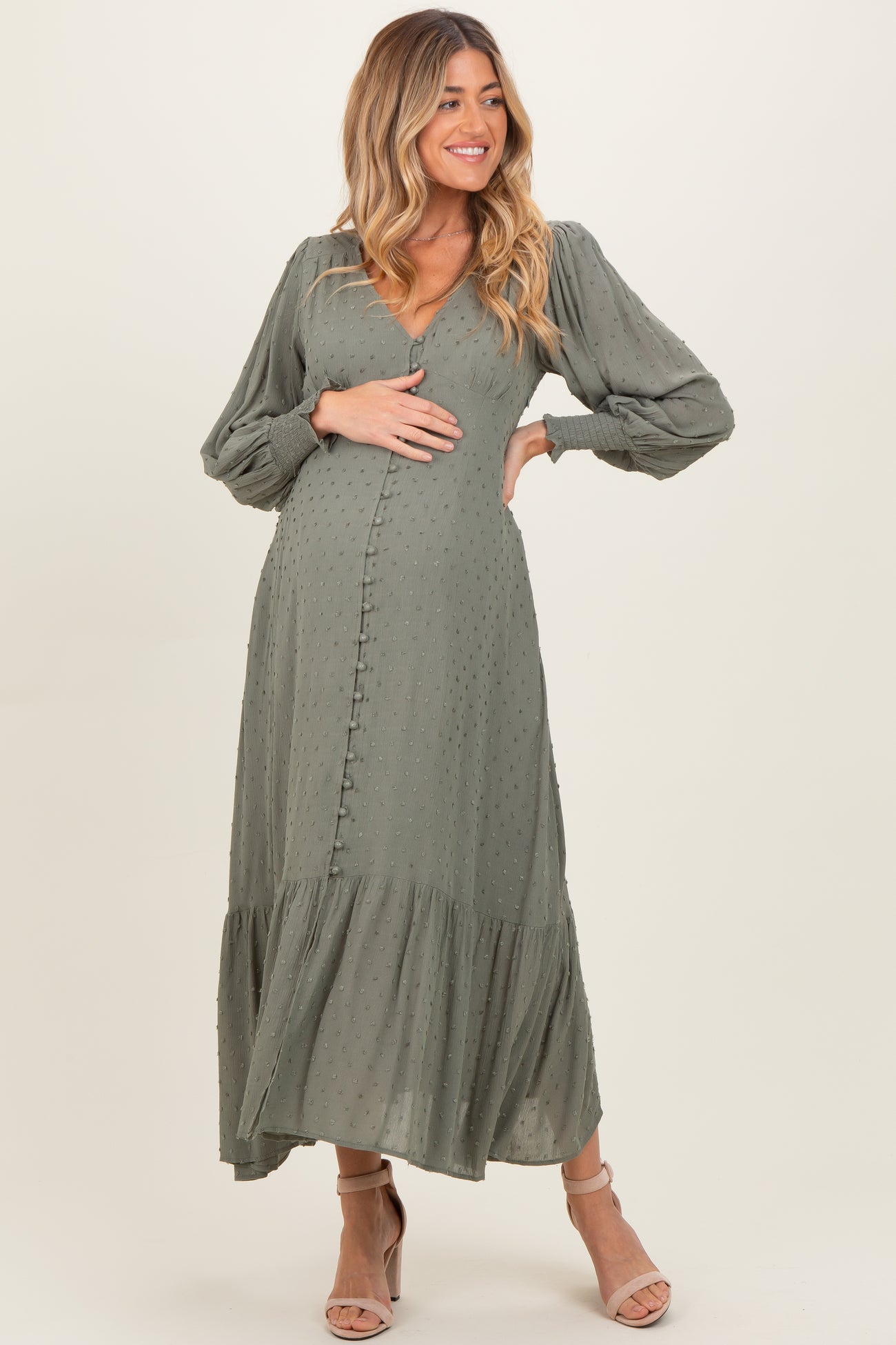 woman wearing a sage green maternity dress with puff sleeves and tiered ruffle hem, holding her baby bump