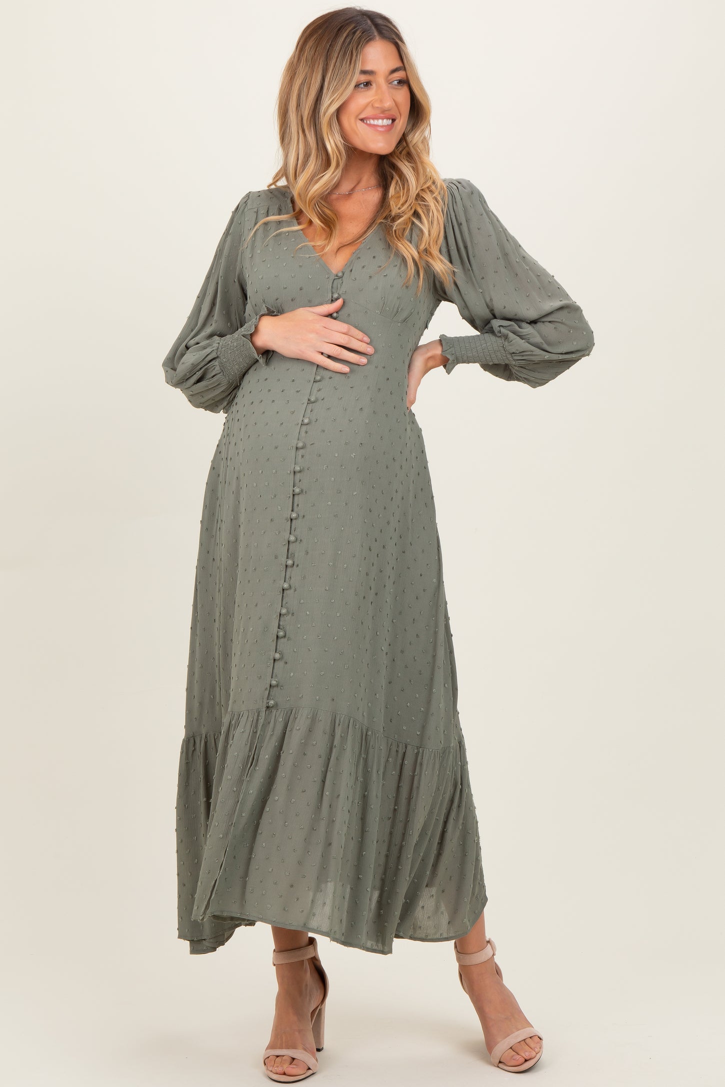 woman wearing a sage green maternity dress with puff sleeves and tiered ruffle hem, holding her baby bump
