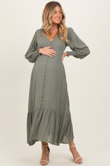 woman wearing a sage green maternity dress with puff sleeves and tiered ruffle hem, holding her baby bump