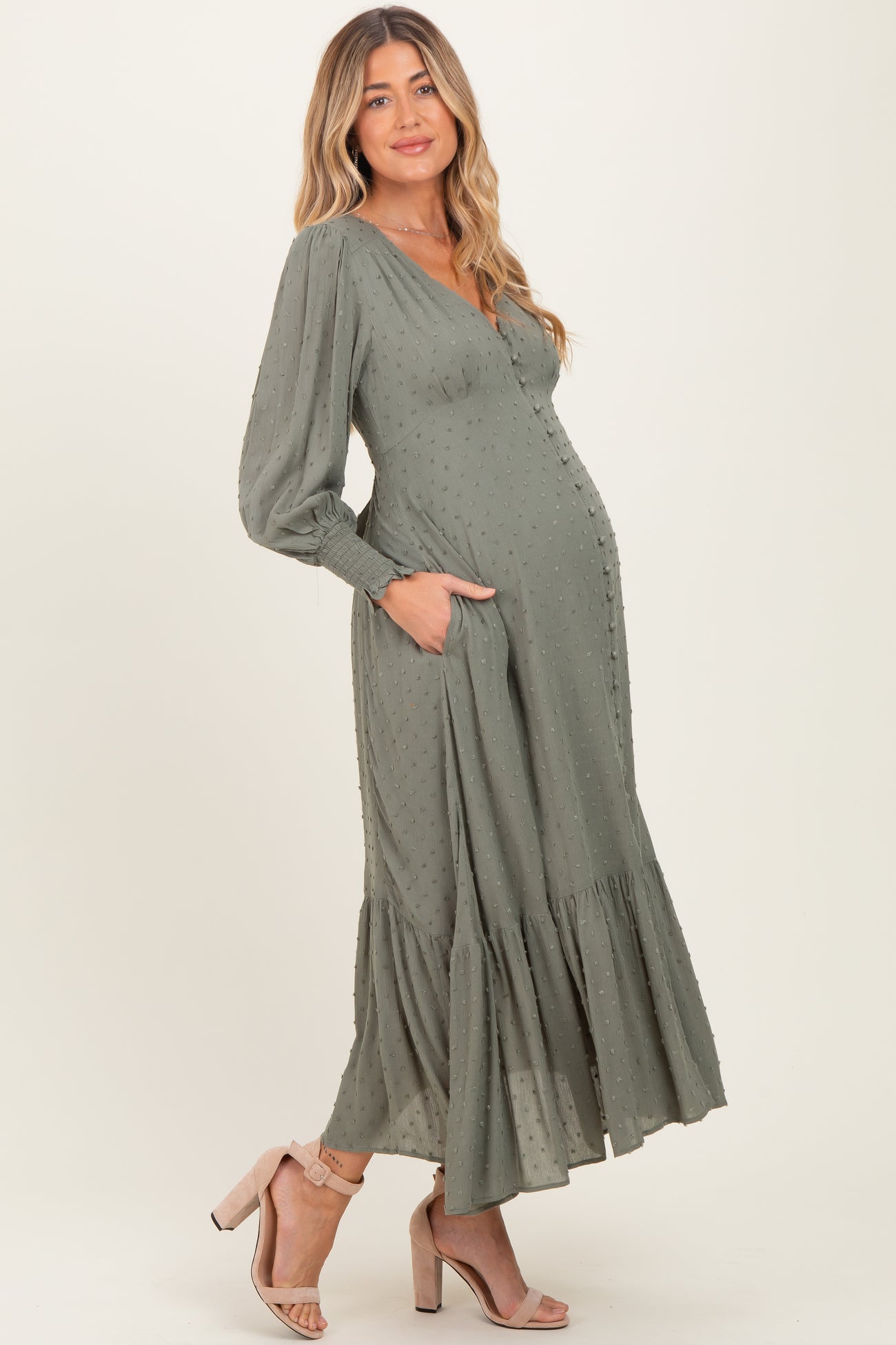 woman wearing a sage green maternity dress with long sleeves, ruffled hem, and pockets, highlighting her baby bump