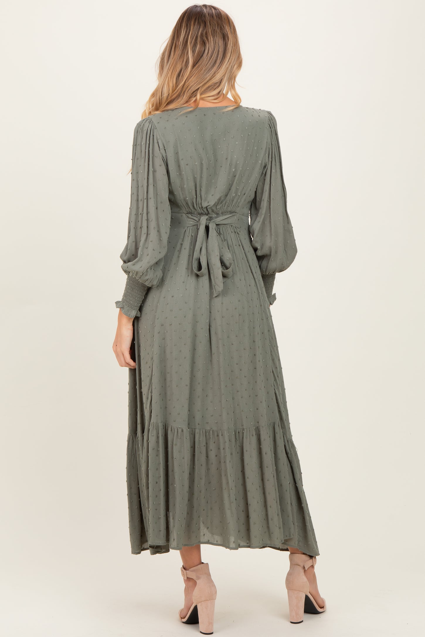 woman wearing a sage green long sleeve maternity dress with a tie-back detail and tiered skirt