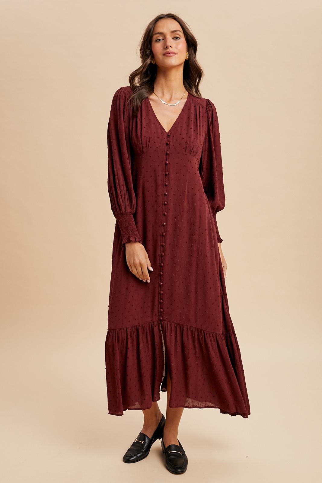 woman wearing a burgundy long sleeve midi dress with a v-neckline and button details, styled with loafers