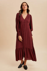 woman wearing a burgundy long sleeve midi dress with a v-neckline and button details, styled with loafers
