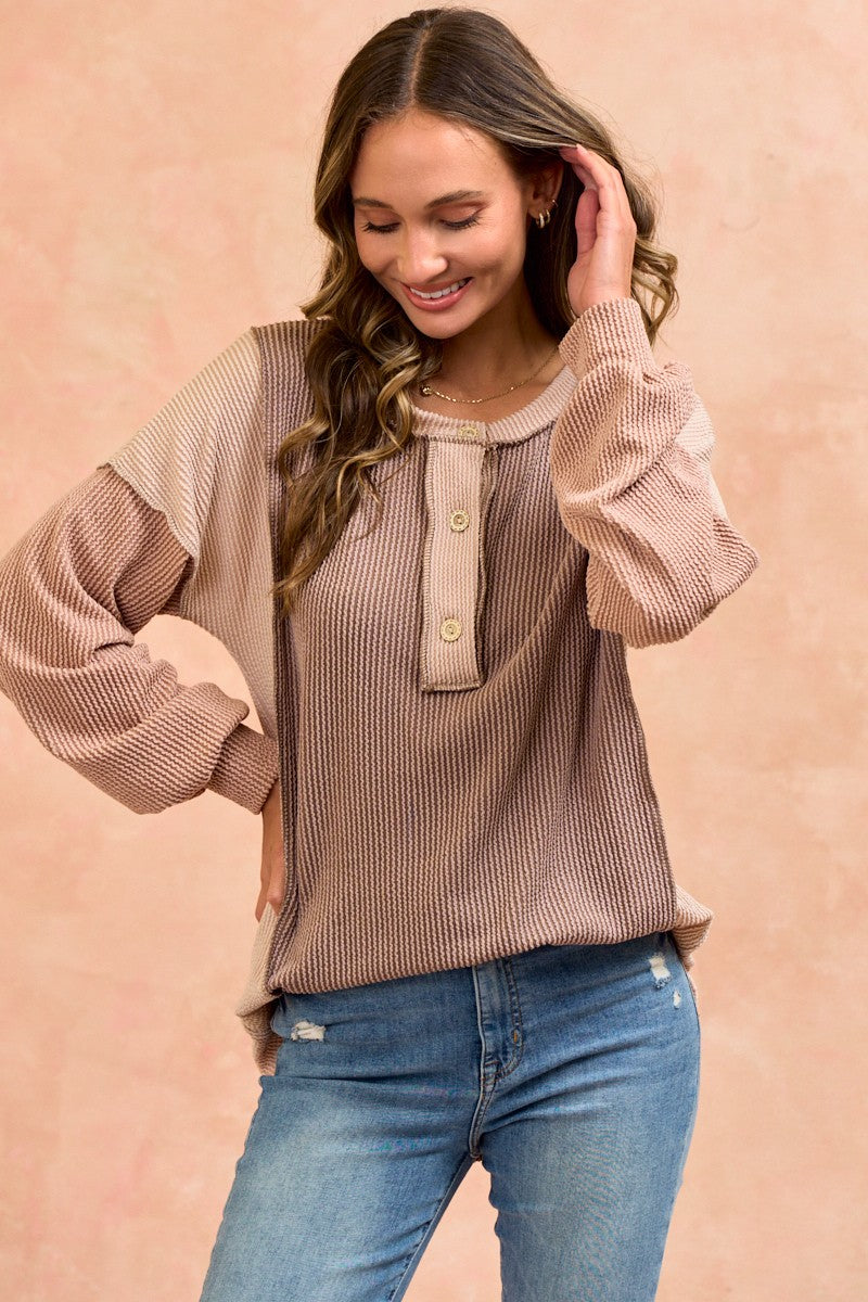 woman wearing a beige and brown color block long sleeve henley top with button details and relaxed fit paired with jeans
