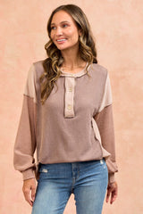 woman wearing a beige and taupe color block long sleeve top with button detailing and loose fit, styled with jeans