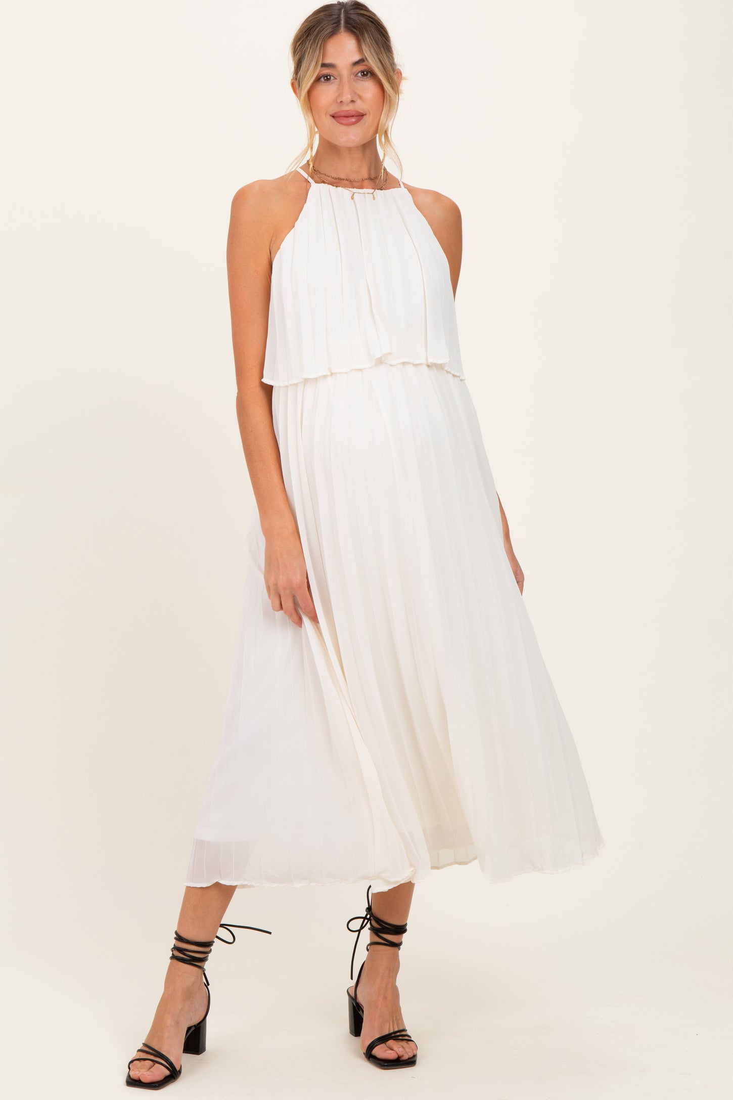 woman wearing a flowy white maternity dress with a halter neckline and tiered bodice, showcasing a baby bump