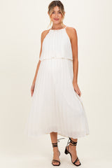 woman wearing a white pleated maternity dress with a halter neckline and a flowy skirt, showing her baby bump