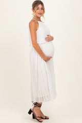woman wearing a white pleated maternity dress and holding her baby bump