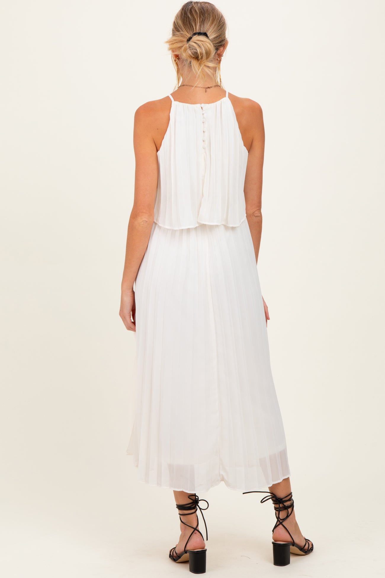 woman wearing a white pleated maternity dress with a halter neckline and layered back, showing a baby bump