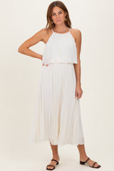 woman wearing a white pleated maxi dress with a halter neckline and layered bodice, standing with one hand on her hip