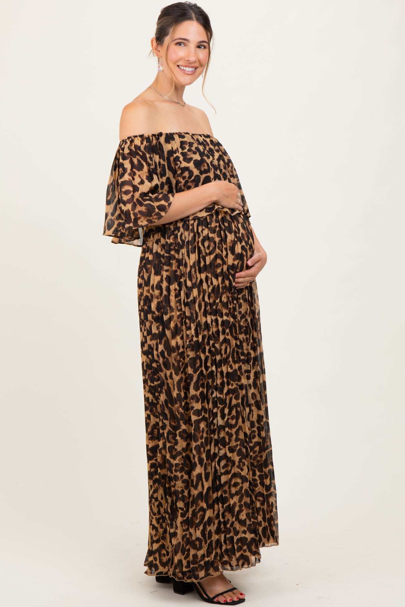 woman wearing a leopard print off-the-shoulder maternity maxi dress and holding her baby bump
