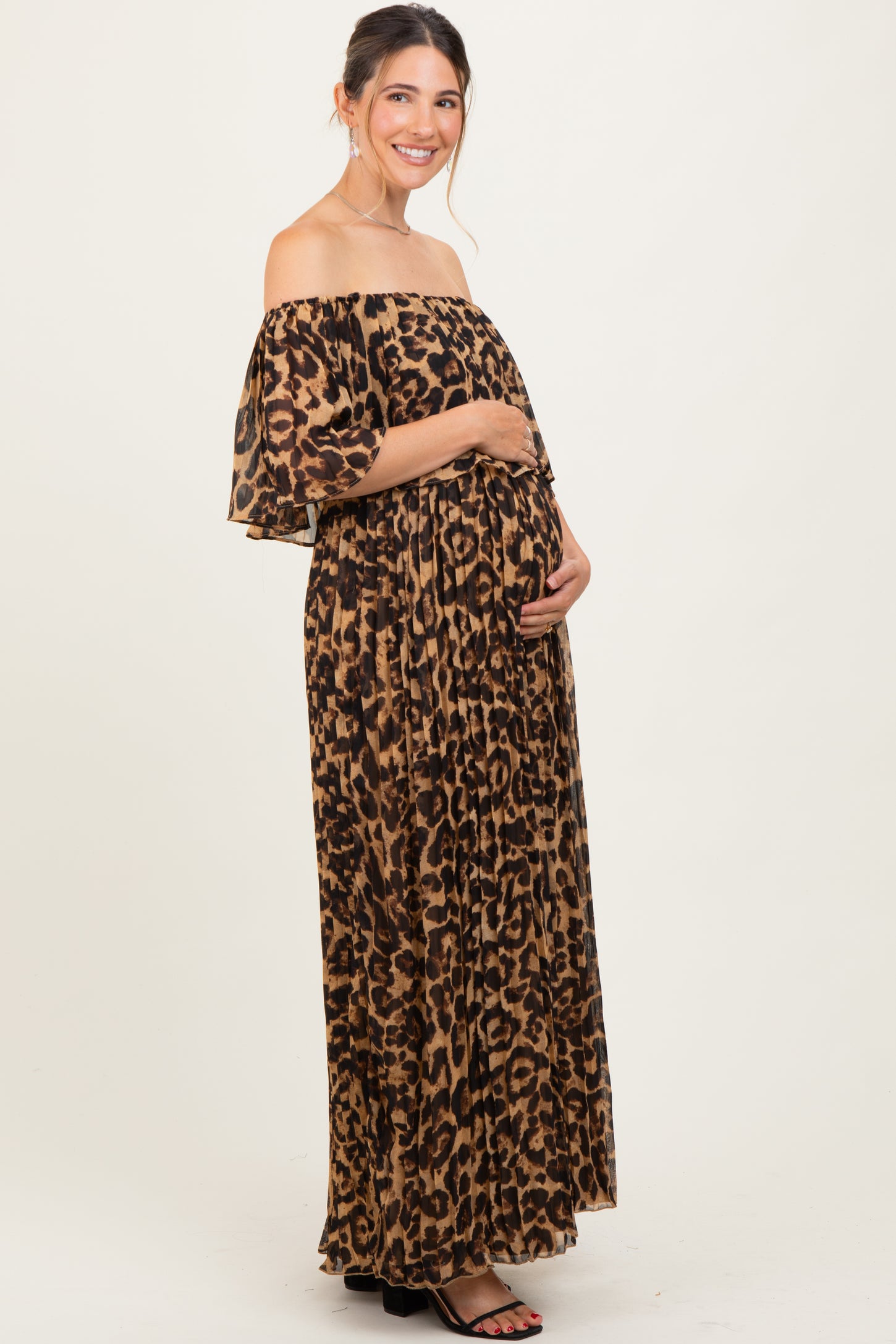 woman wearing a leopard print off-the-shoulder maternity maxi dress and holding her baby bump