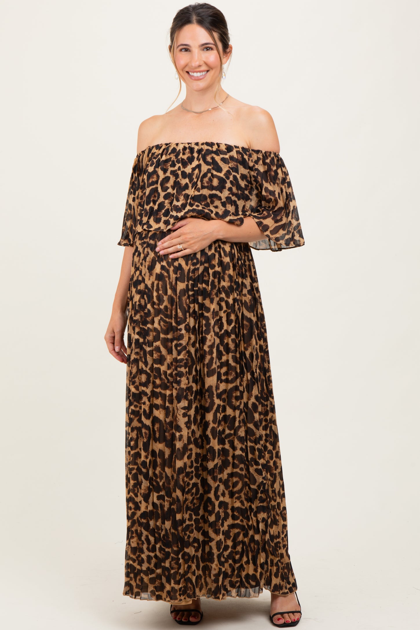 woman wearing a brown leopard print off-shoulder maternity maxi dress and holding her baby bump