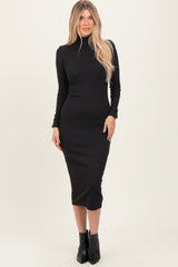 woman wearing a black long sleeve turtleneck midi dress with a form-fitting silhouette and black ankle boots