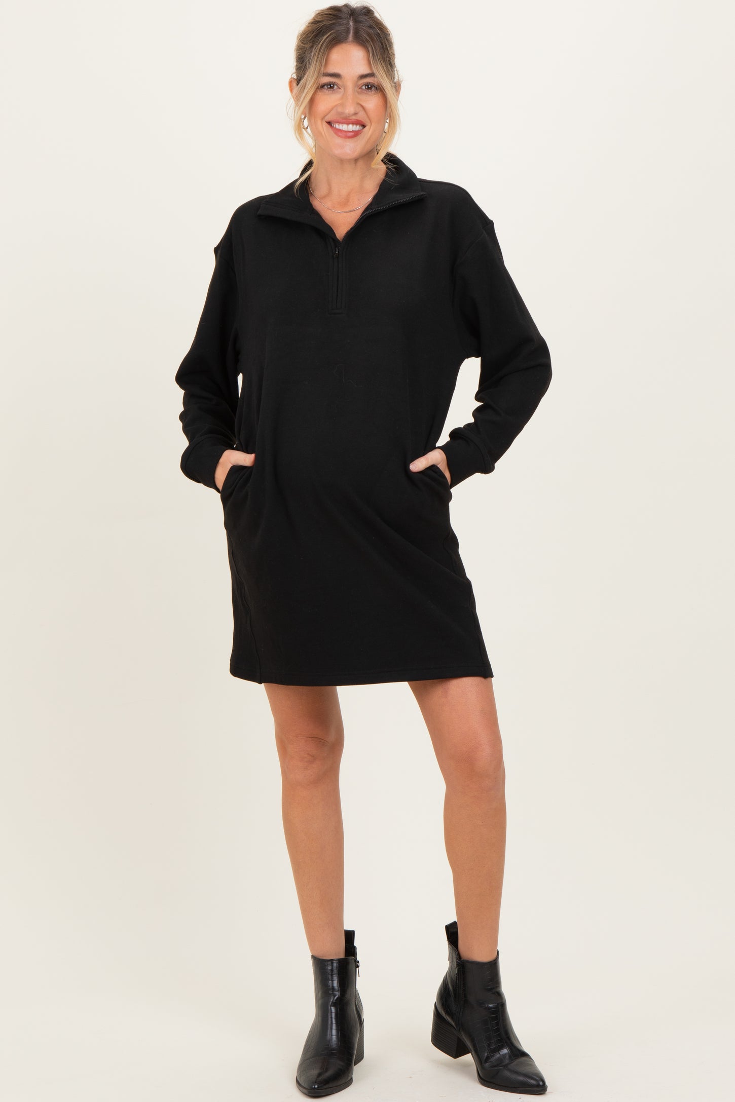 woman wearing a black maternity pullover dress with a quarter zip and two front pockets