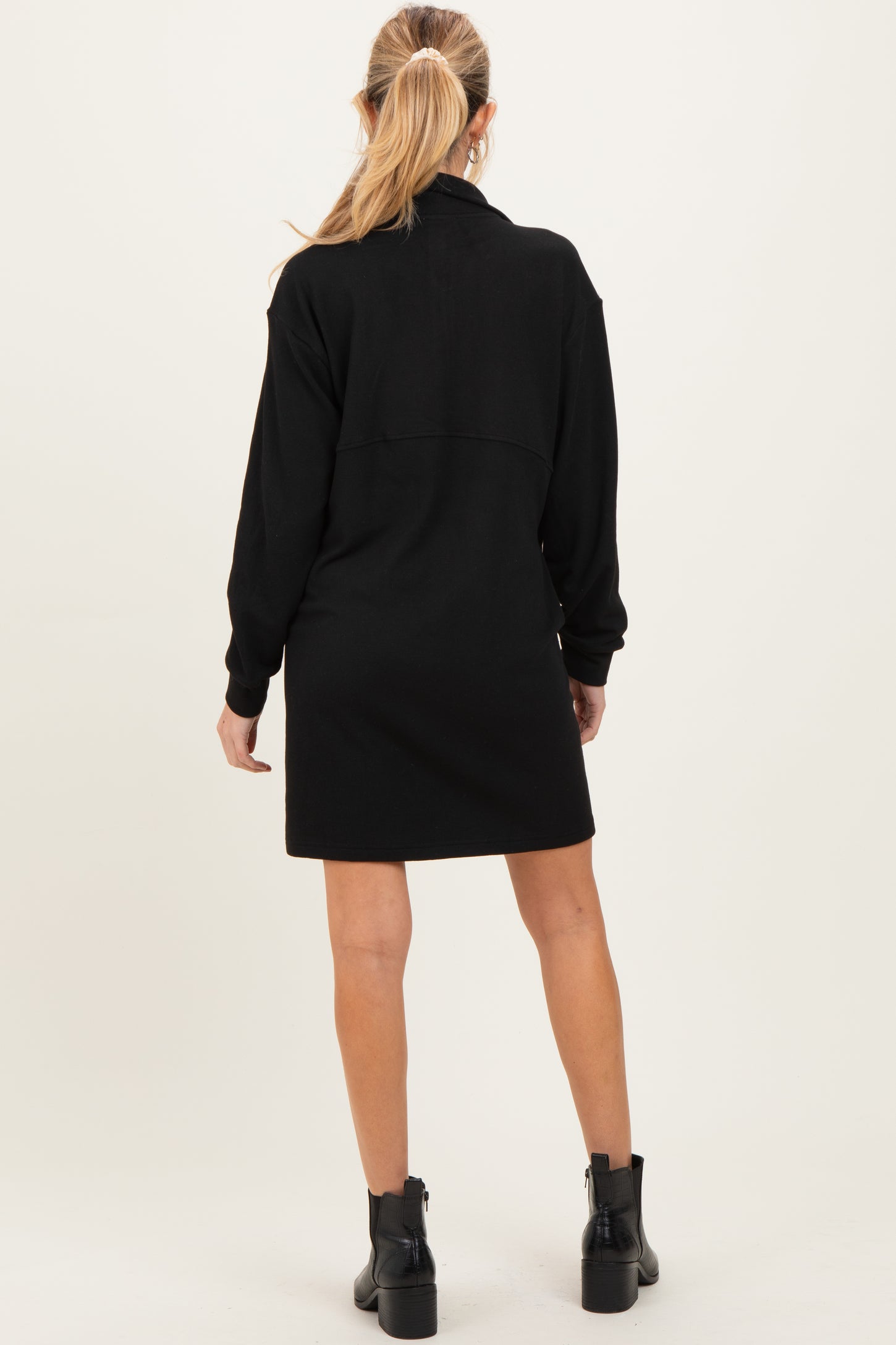 woman wearing a black maternity dress with long sleeves and a back yoke detail, showing her back while standing