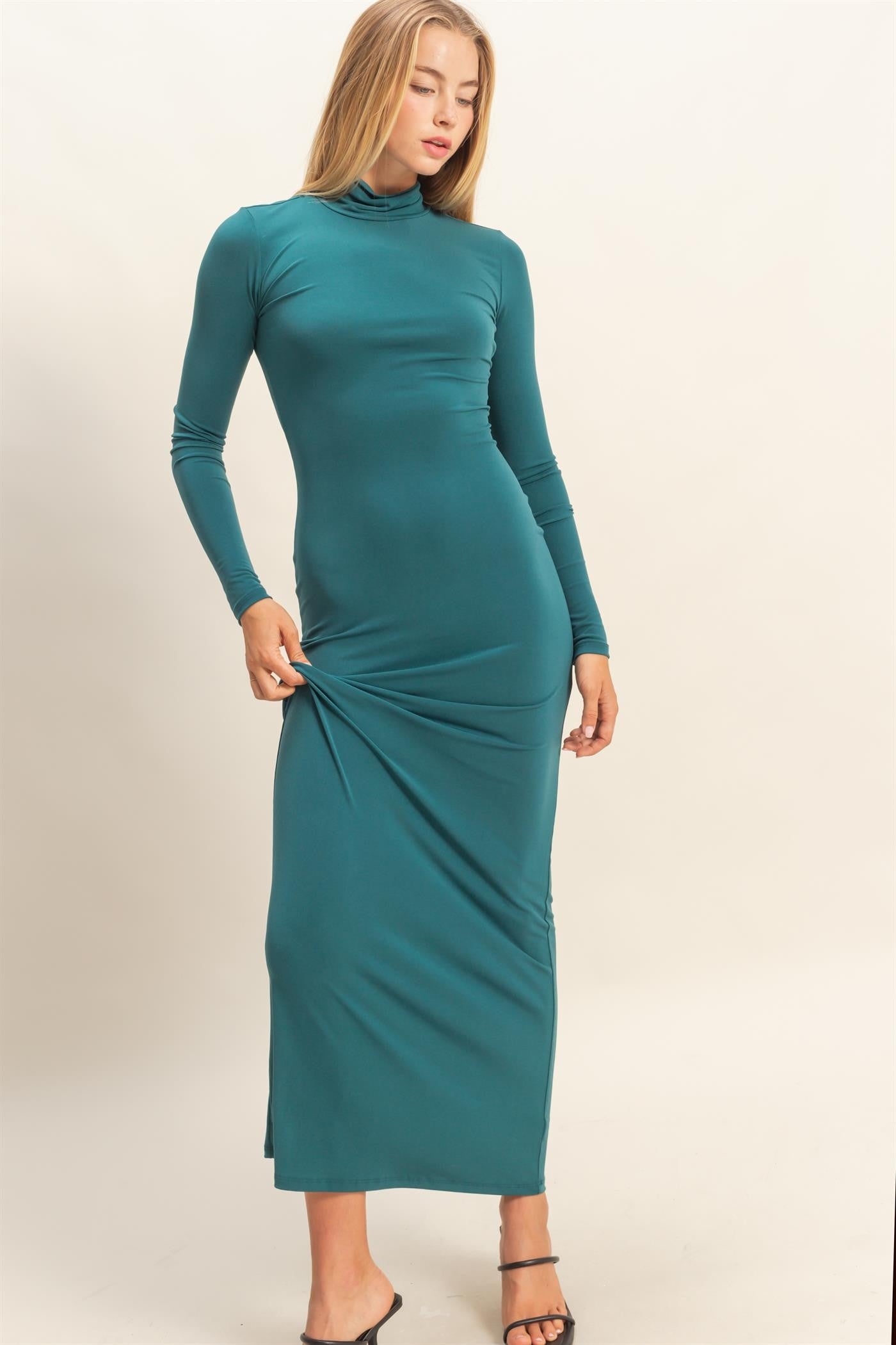woman wearing a teal long sleeve fitted maxi dress with a high neck and side slit