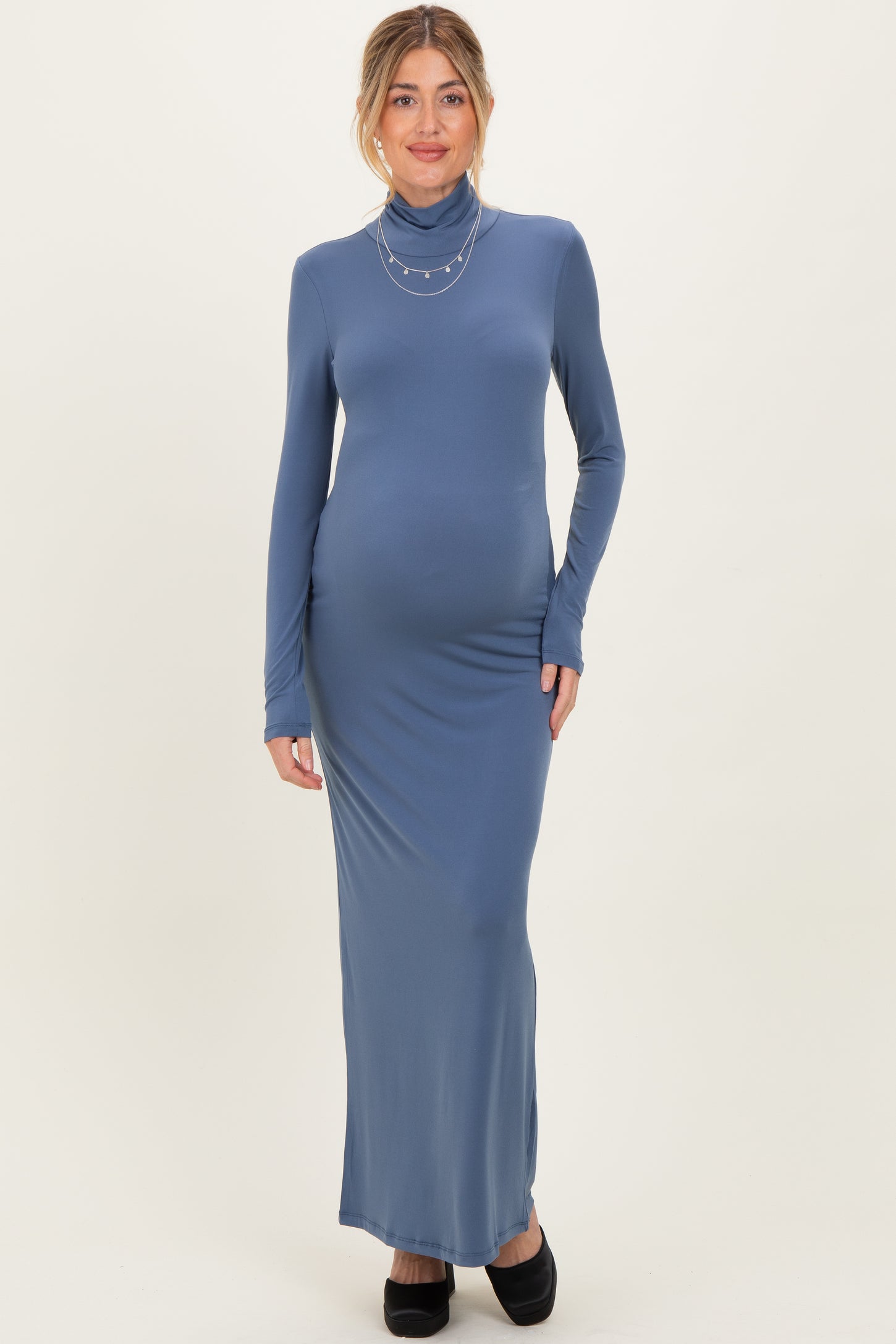 woman wearing a blue long sleeve maternity dress with a turtleneck and a visible baby bump