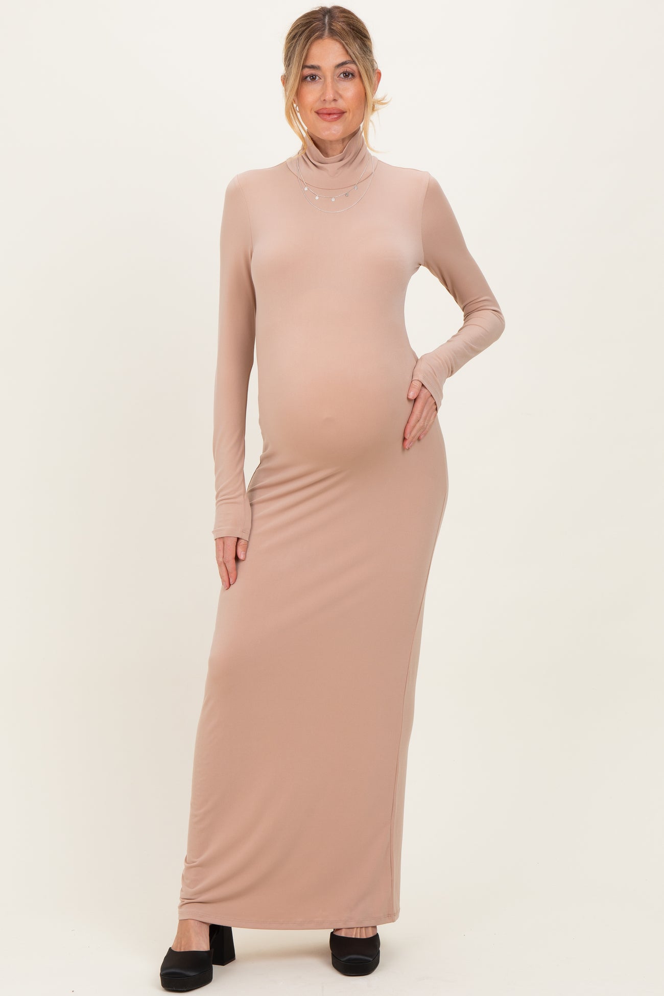 woman wearing a light beige maternity maxi dress with long sleeves and a mock neck, showing her baby bump