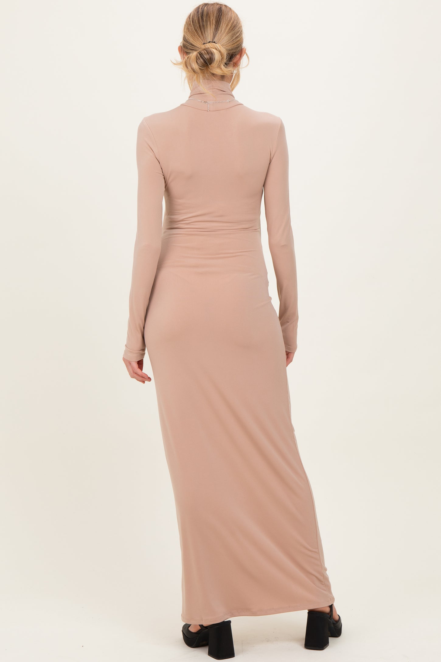 woman wearing a long sleeve beige maternity dress with a fitted silhouette and a floor-length design