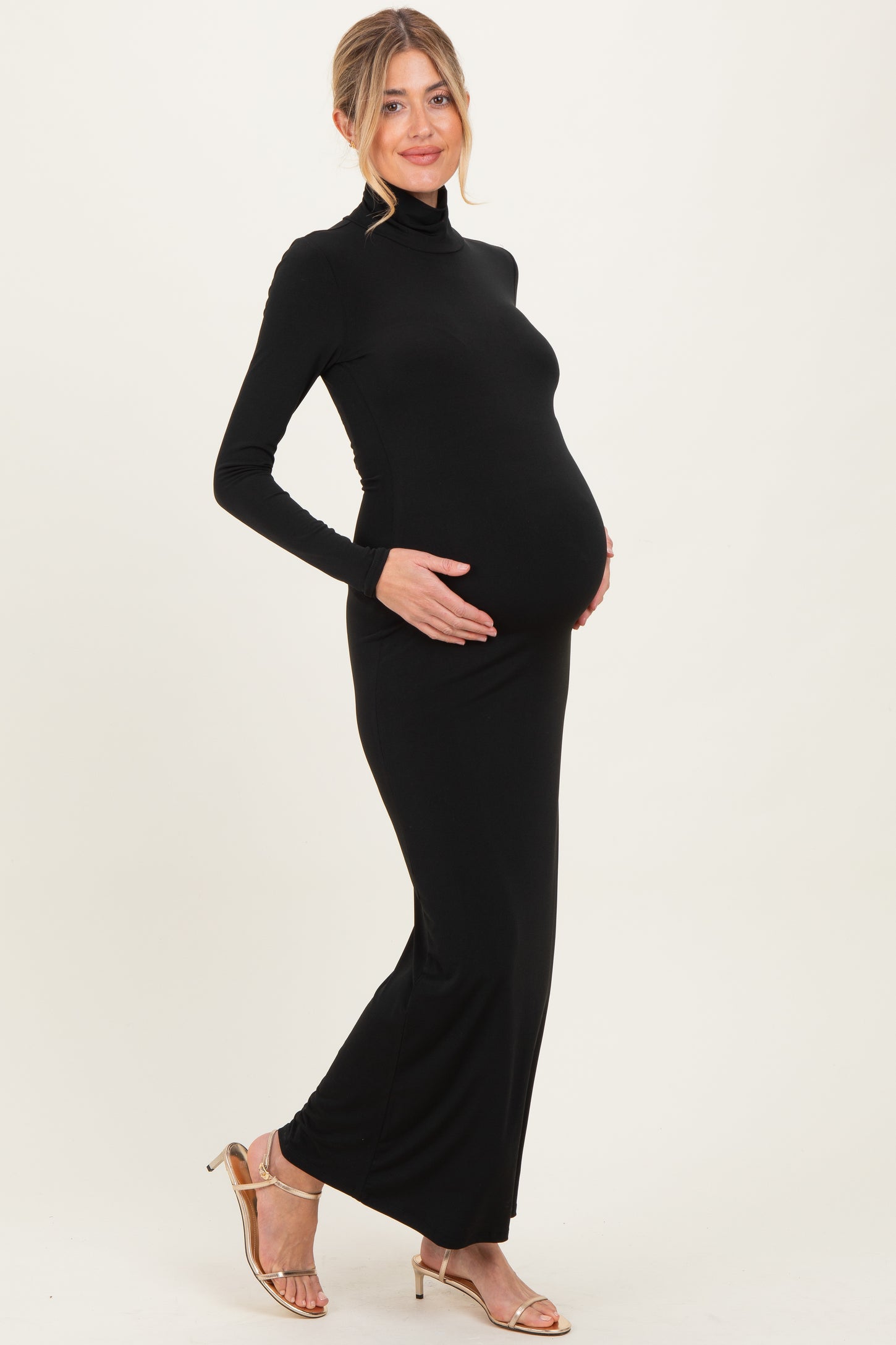 woman wearing a black long sleeve maternity dress with a fitted silhouette and holding her baby bump