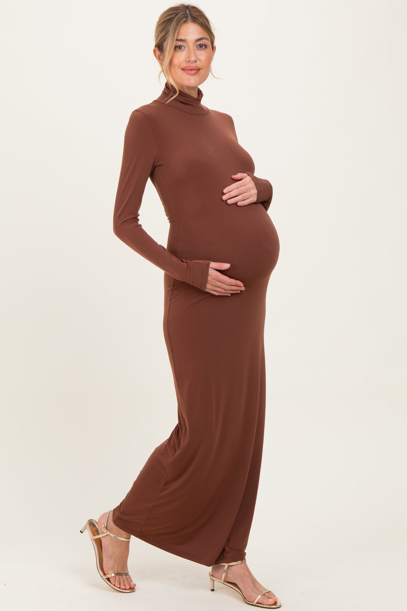 woman wearing a brown long sleeve maternity dress, holding her baby bump and smiling