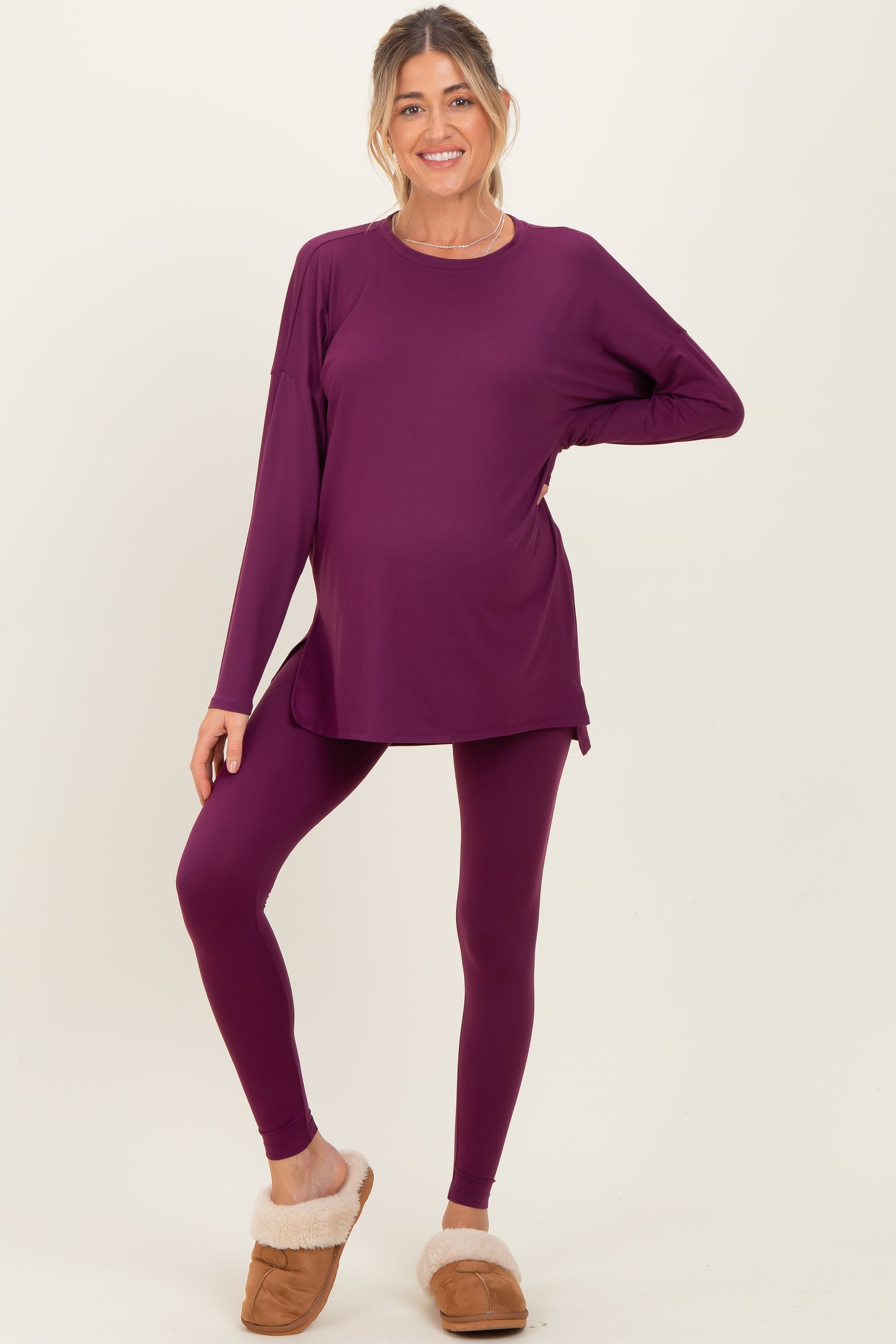 woman wearing a purple long sleeve maternity top and matching leggings, showing her baby bump, paired with cozy slippers